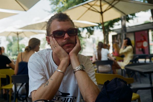 A person at a cafe table wearing dark sunglasses, looking toward the camera