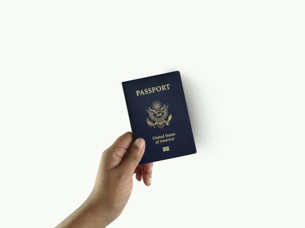 A hand holding a United States passport against a plain background
