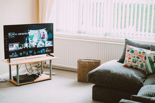 A flat-screen smart TV on a low stand in a bright living room, showing a streaming app's home screen, with an empty couch beside it