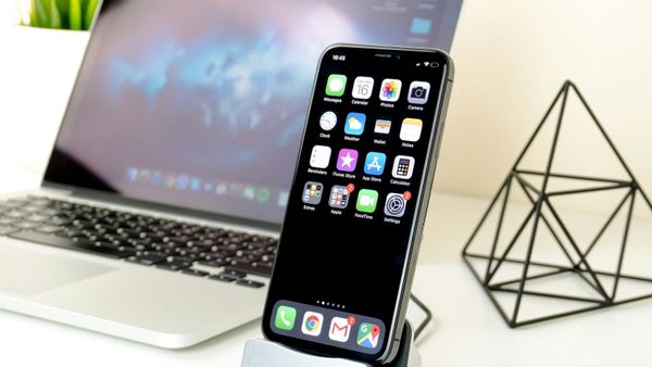 An iPhone home screen of built-in apps standing next to a laptop.
