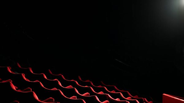Rows of empty red seats in a dark movie theater, lit by a single projector beam