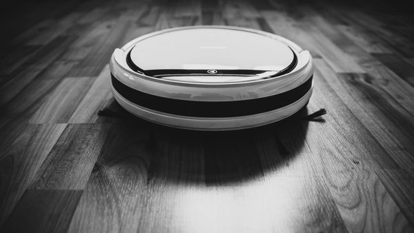 A robot vacuum sitting on a hardwood floor, photographed in black and white
