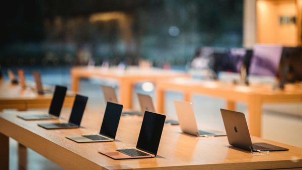 A row of laptops open on a wooden display table in a computer store.