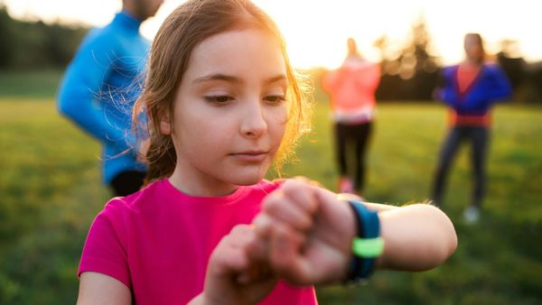 A girl in a pink shirt checking the smartwatch on her wrist in a field at sunset