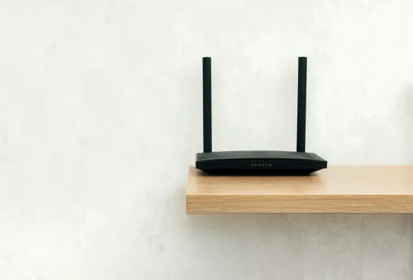 A black Wi-Fi router with two antennas sitting on a wooden wall shelf.