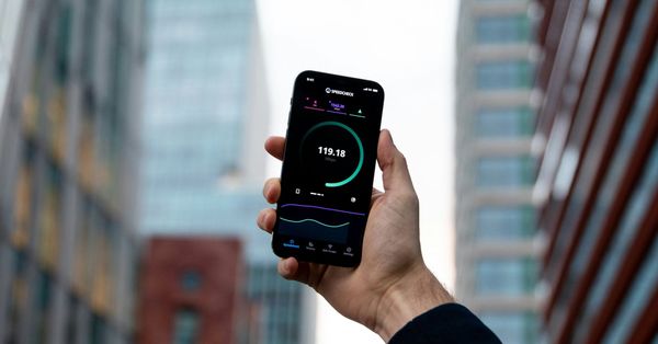 A hand holding a phone that is running an internet speed test, showing a result of 119 Mbps.