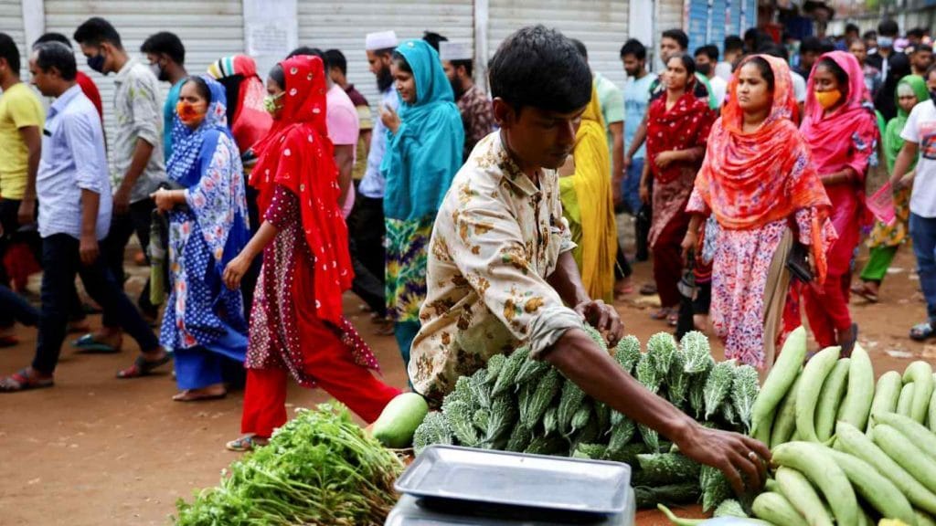 A man sells vegetables while garment workers leave a factory in Dhaka. Photo: Reuters via Nikkei Asia