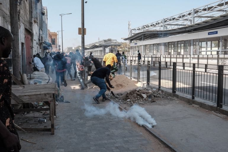 Protesters run away as a smoke grenade lands near them during clashes with police in Dakar. Photo: Guy Peterson/AFP