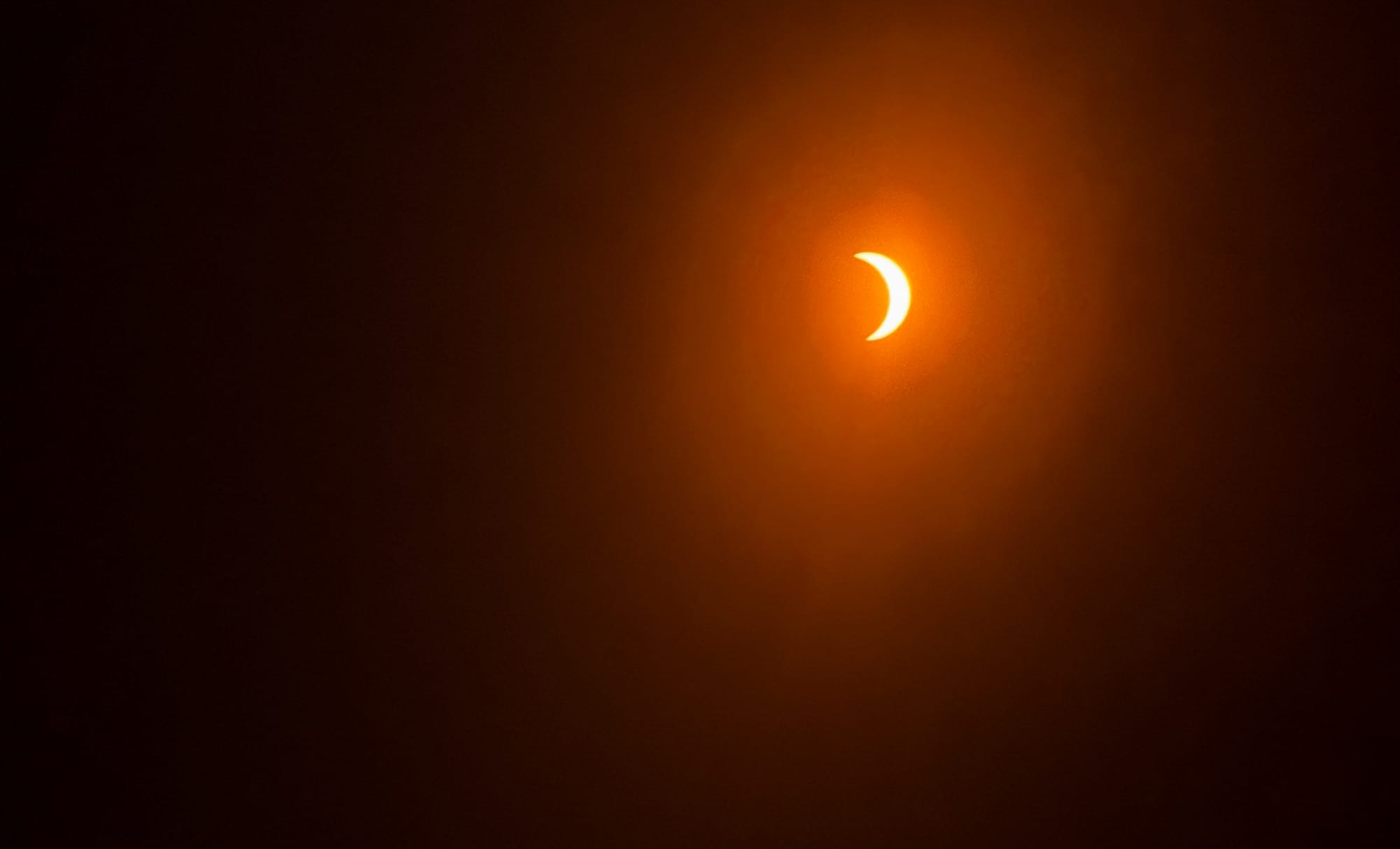 A photo, shot through the glasses filter, of the eclipse. The sun is a crescent, almost completely covered by the moon. 