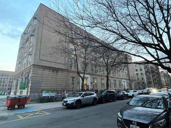 A large brick school building on a New York City street in early spring. 