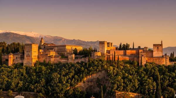 The Alhambra palace complex in Granada, Spain at golden hour with the snow-capped Sierra Nevada mountains in the background