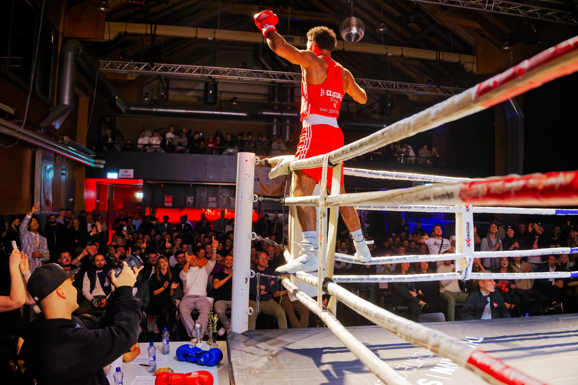 Alpha Amadou Käser im roten Boxdress auf den Ringseilen vor dem Publikum