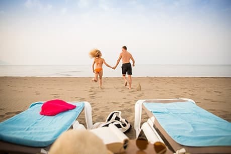 Paar läuft am Strand zum Meer, im Vordergrund Wassersportausrüstung