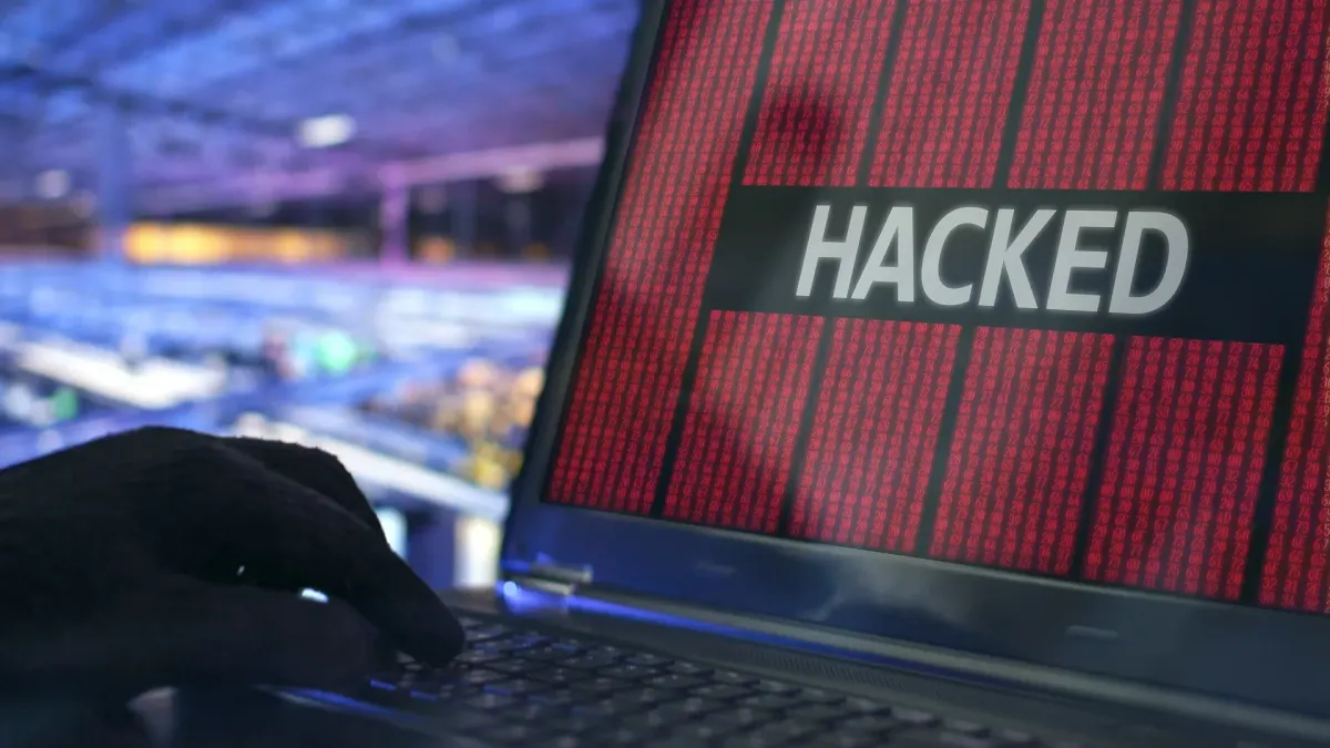 Eine dunkel gekleidete Person arbeitet an einem Laptop in einem abgedunkelten Raum