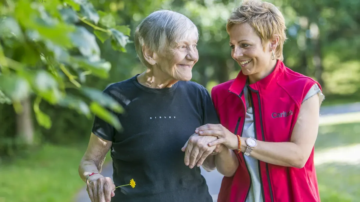 Eine freiwillige Besucherin begleitet eine ältere Patientin in der Geriatrie