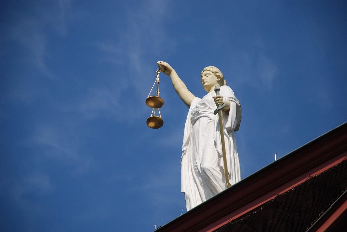 Symbolbild: Weiße Justitia-Statue mit Waage und Schwert vor blauem Himmel