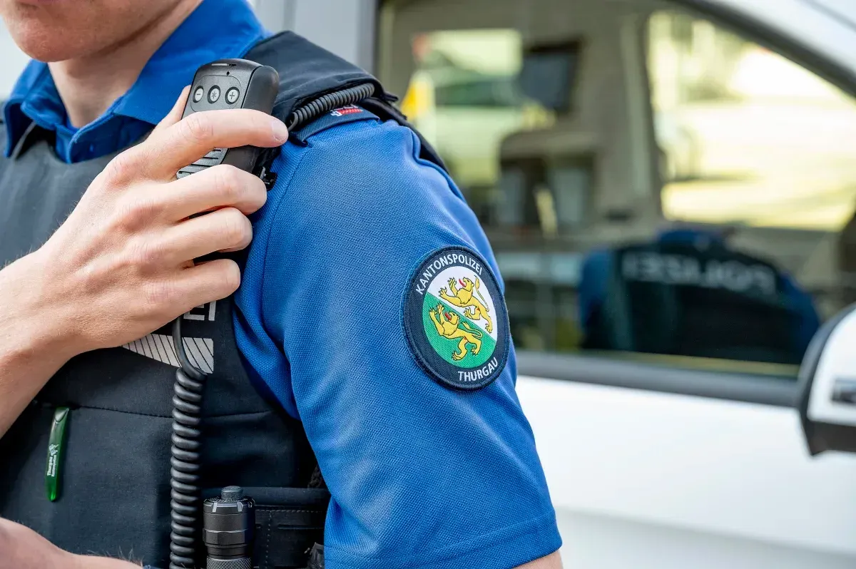 Ein Polizist der Kantonspolizei Thurgau hält ein Funkgerät vor einem Polizeifahrzeug. Das Emblem ist deutlich sichtbar.