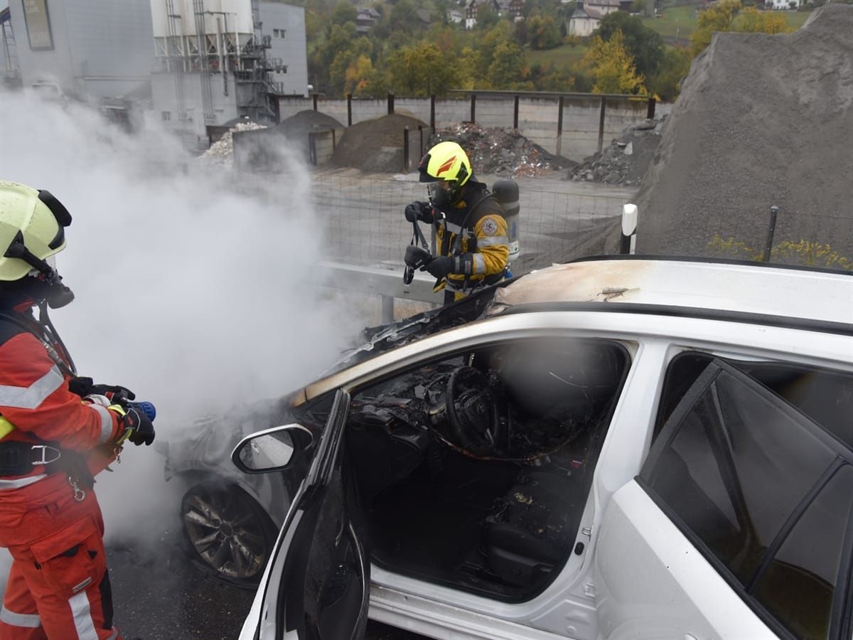 Zwei Feuerwehrleute bekämpfen den Fahrzeugbrand auf der A13. Im Hintergrund ein Gebäude des Kieswerks Maienfeld neben der A13.