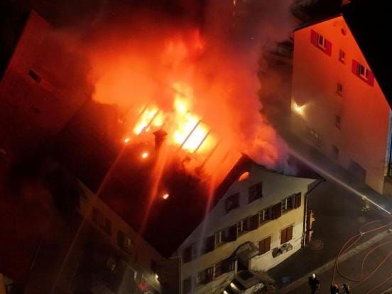 Ein Mehrfamilienhaus, dessen Dachstock in Vollbrand steht.