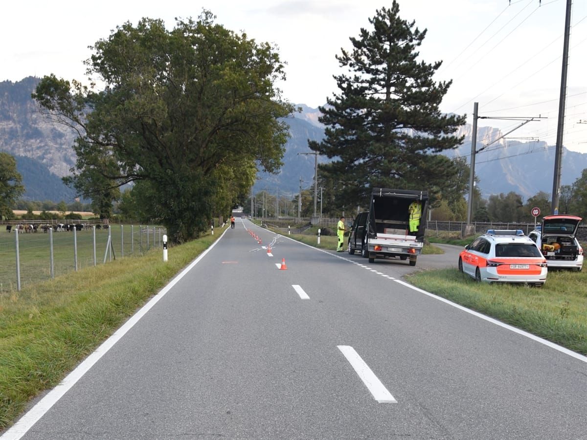 Rechts der Strasse zwei Polizeiautos und ein Drittfahrzeug. Auf der Strasse eingezeichnete Unfallspuren.
