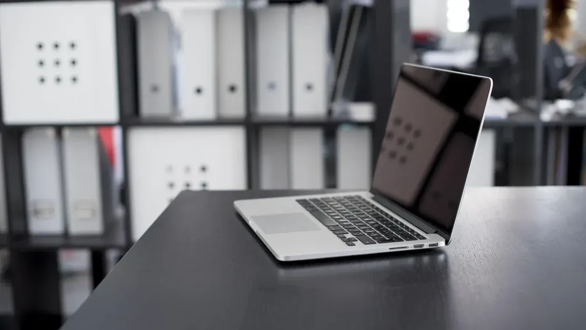 Laptop auf einem aufgeräumten Schreibtisch vor Büroregalen