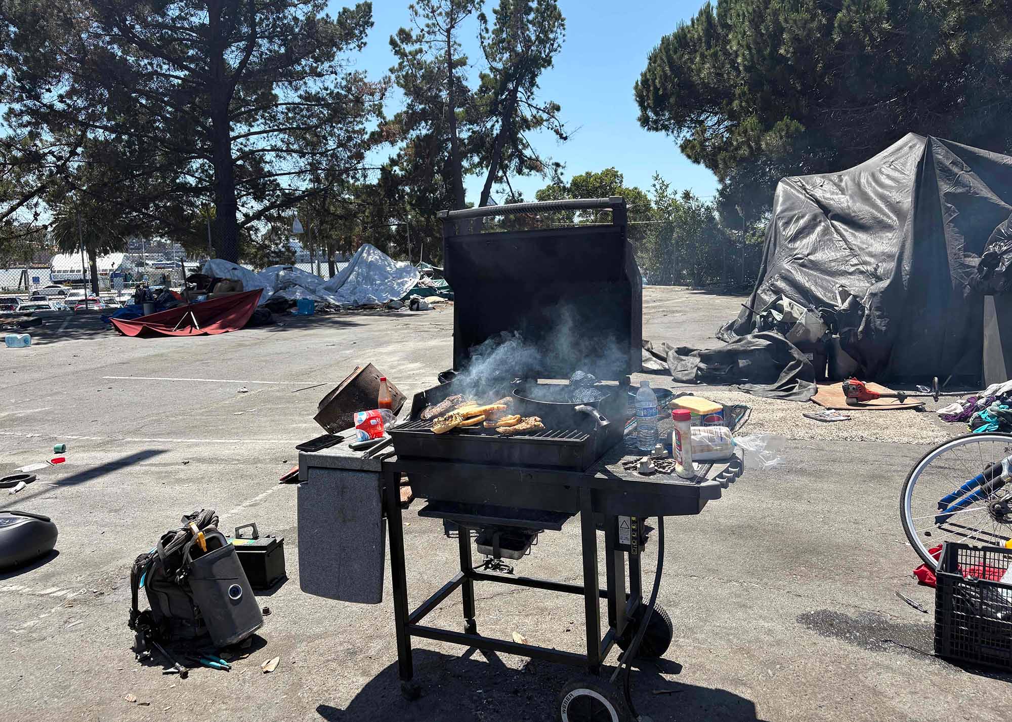 A grill stands with cooking meat and bread in an encampment in the Vallejo Ferry Terminal parking lot area in Vallejo. 