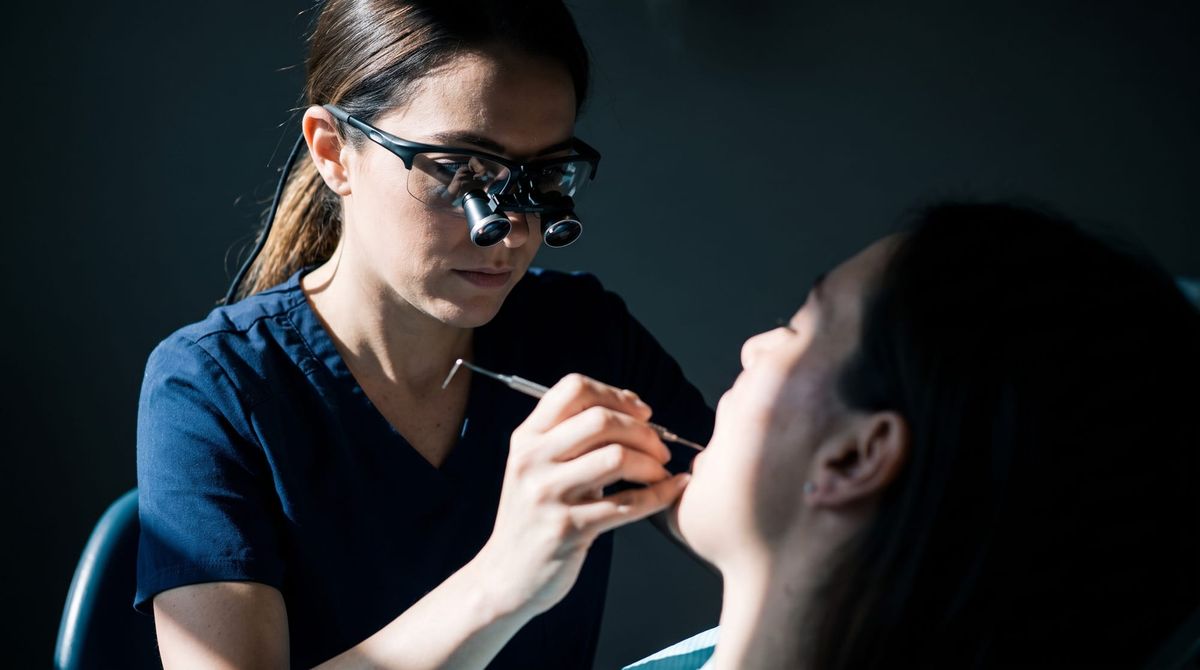 A dental hygienist at chairside examining a patient's gums with a periodontal probe