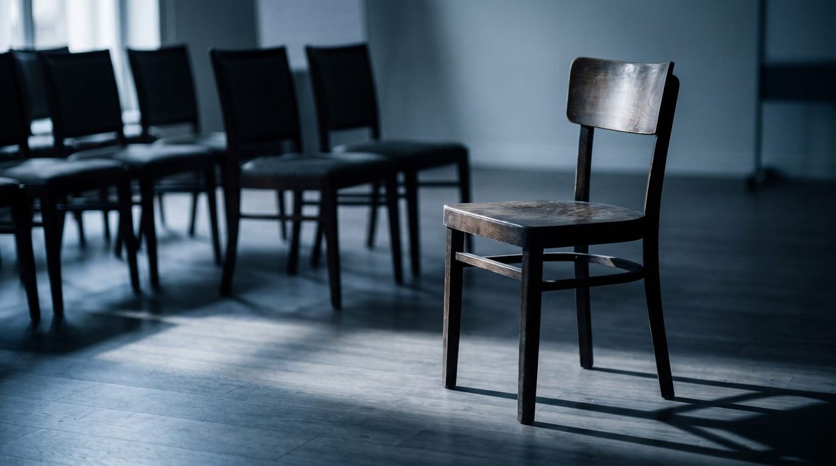 A single empty wooden chair kept open at the end of a row, in soft window light