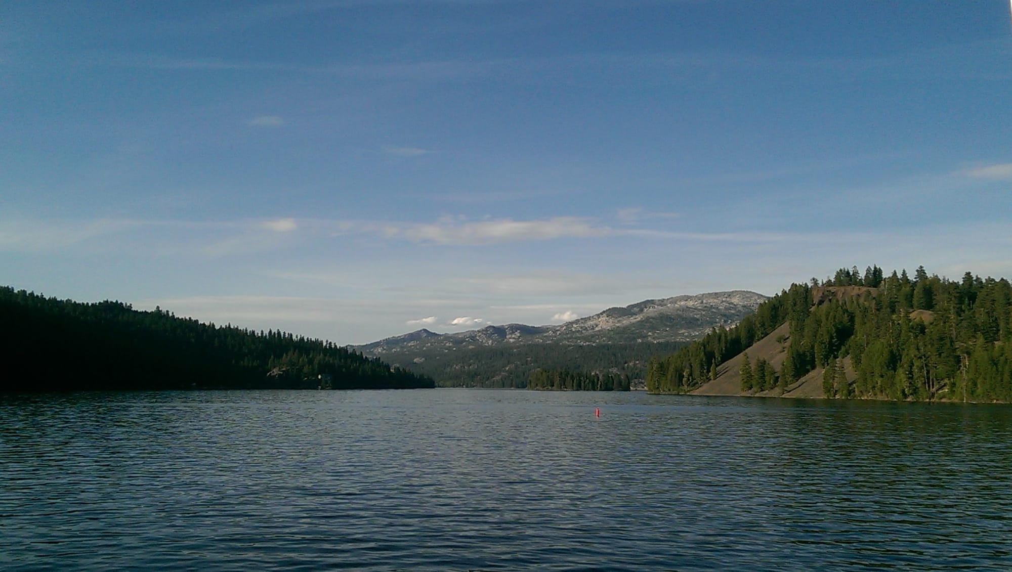 A dark-blue lake. off in the distance, mountains covered in ponderosa pine trees.
