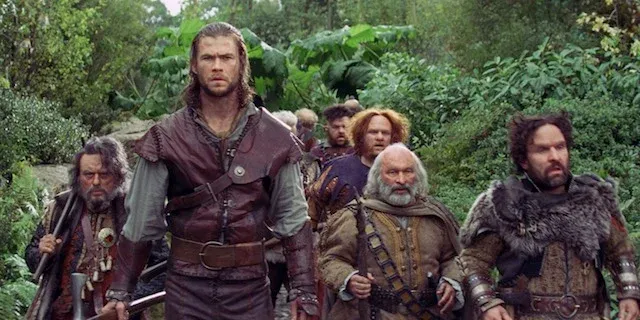 A typically-heighted huntsman walks through a forest flanked by smaller-portioned people that are clearly not dwarfs.