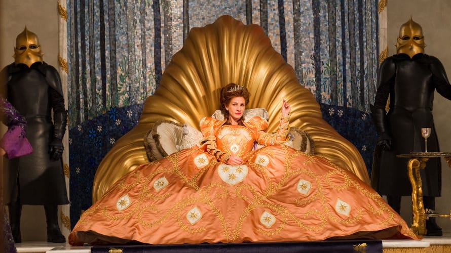 A queen snaps her fingers. She wears a peach-colored dress with golden garland lacework and gold-white stars. She sits on a throne of gold cast to look like its spouting. A side table on which sits a goblet also has legs made of gold, as do the masks of the guard on either side. This is offset with their uniforms, all black, and a blue mosaic backdrop with flowers rising from the floor.