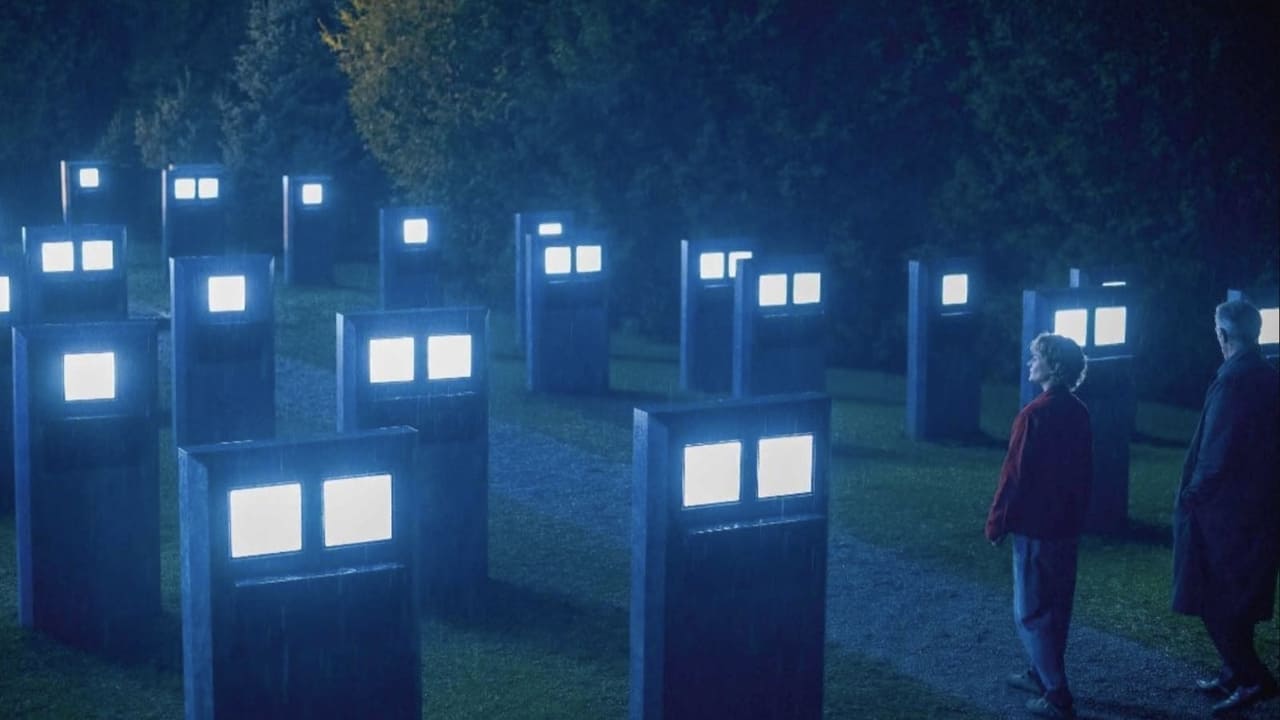 At night, a woman and a man in a cemetary, with rows of shoulder-high tombstones with screens that glow white.
