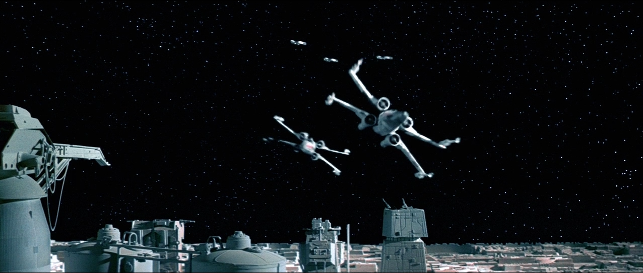 Two X-wing spacecraft fly low over the surface of the Death Star, with three Y-wings bringing up the rear