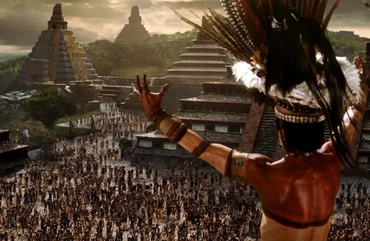 A Mayan chieftain,stands high above a crowd of his people, arms aloft. In the distance stand multiple pyramids.