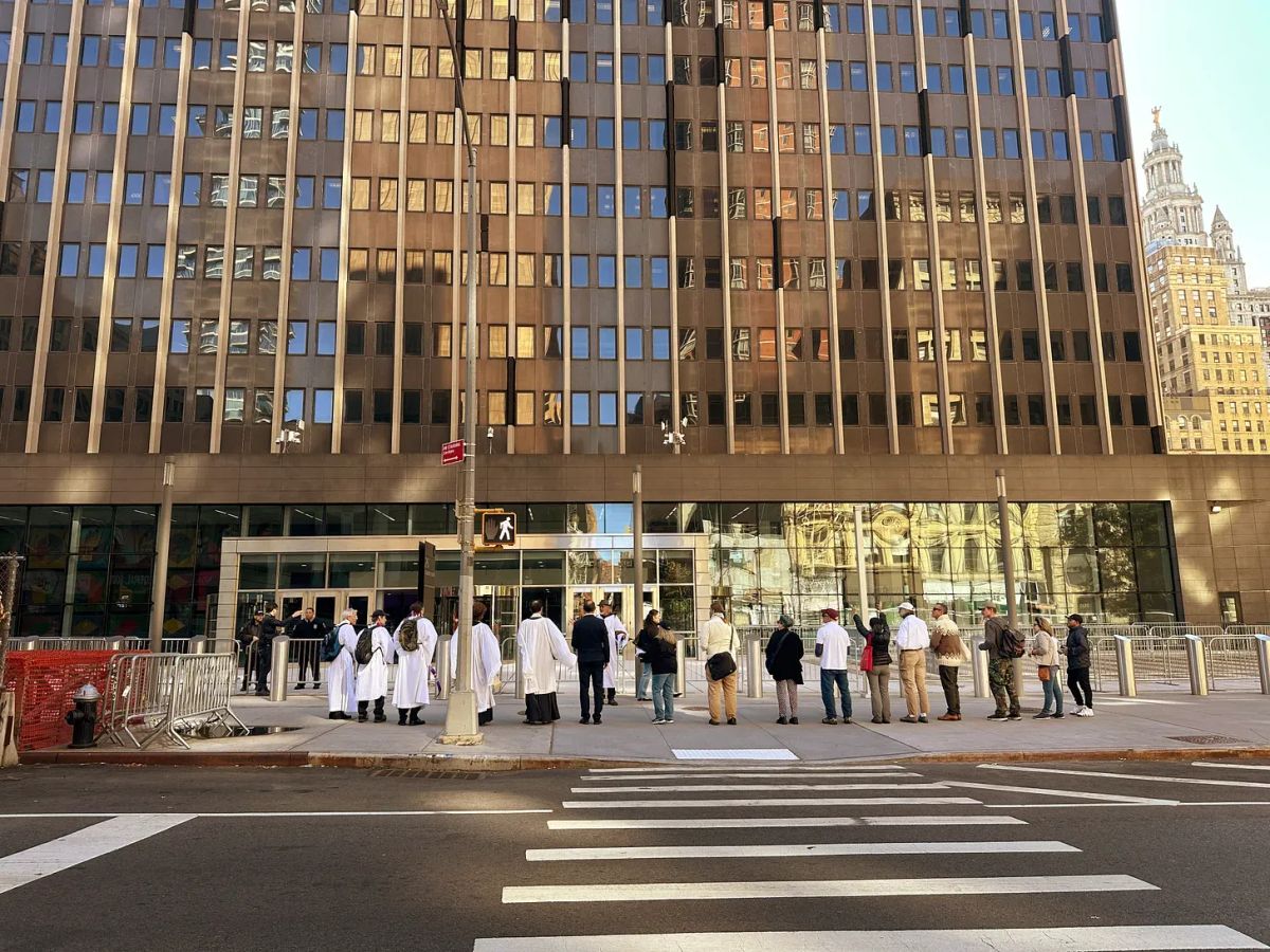 A line of people, including some clergy, stand outside a 26 Federal Plaza, a tall building