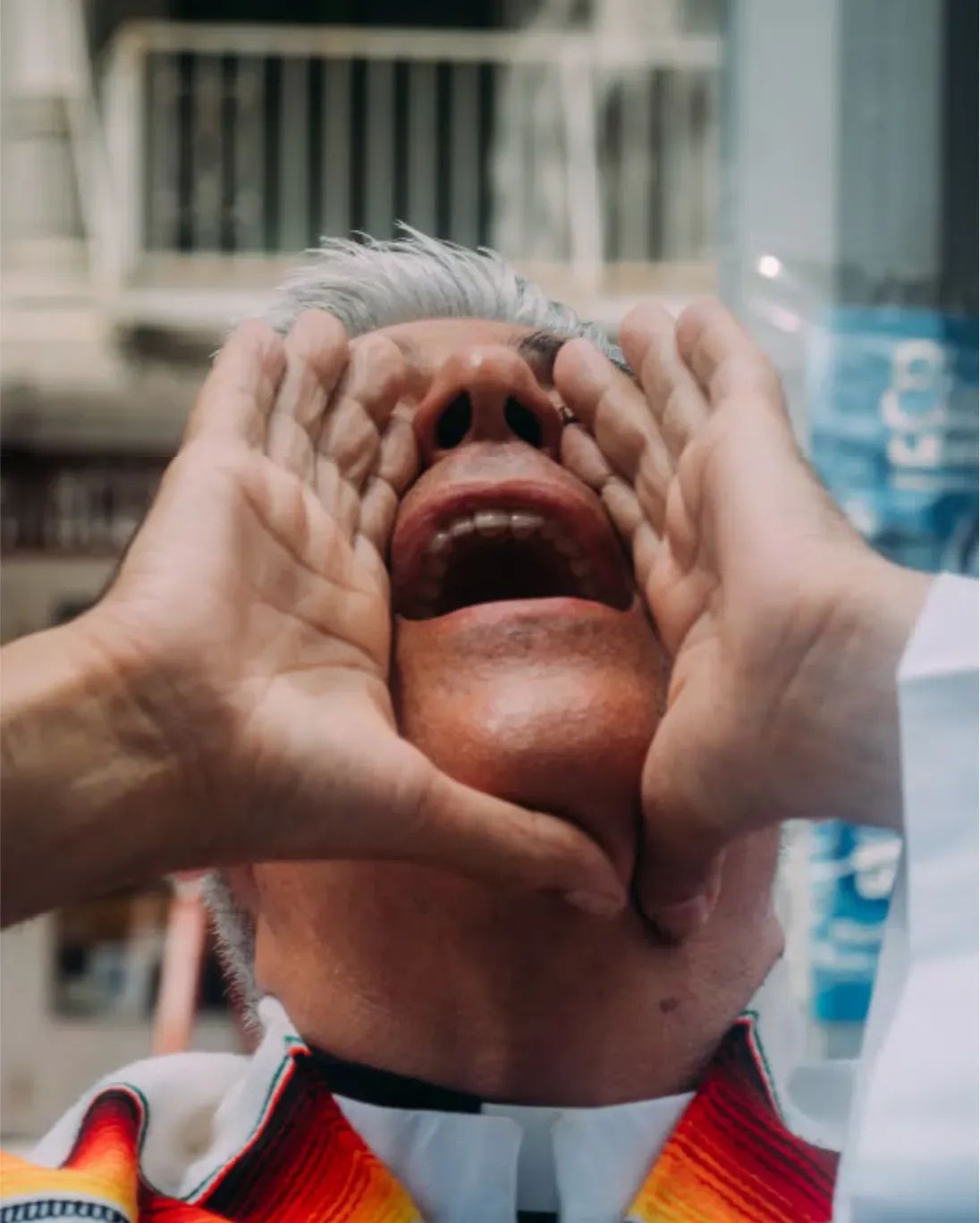 Cluse up of a man with his head back, yelling out with his hands cupped around his mouth. He is wearing a priest's collar