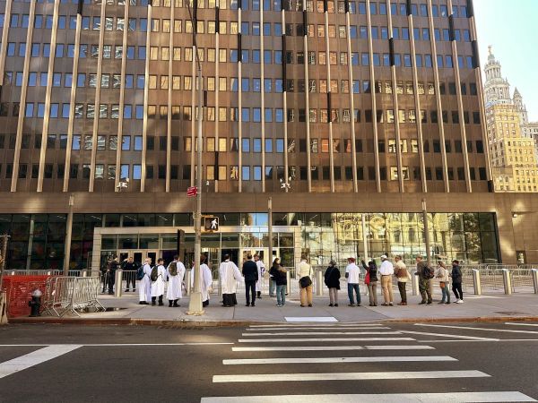 A line of people, including some clergy, stand outside a 26 Federal Plaza, a tall building