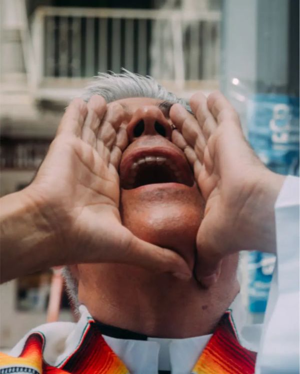Cluse up of a man with his head back, yelling out with his hands cupped around his mouth. He is wearing a priest's collar