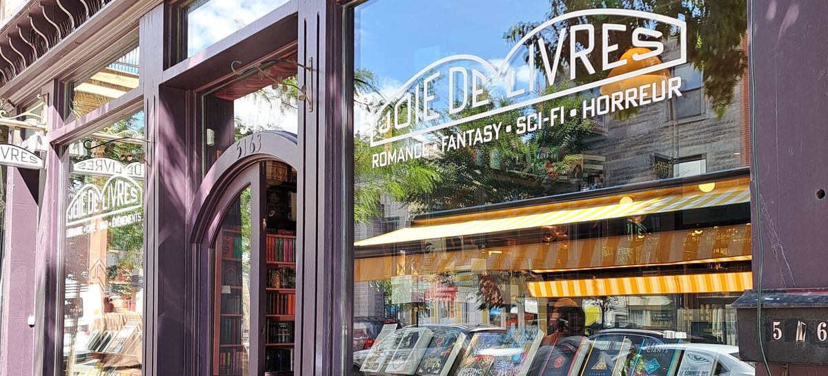 The windows of a bookstore called Joie de Livres, advertising romance, fantasy, sci-fi, and horror.