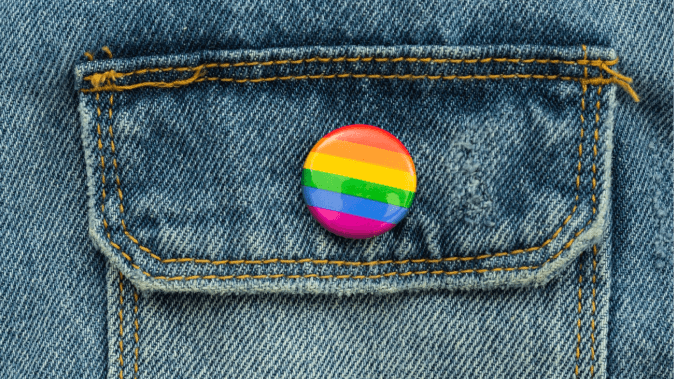 An image of a rainbow pin on top of a jeans jacket pocket.