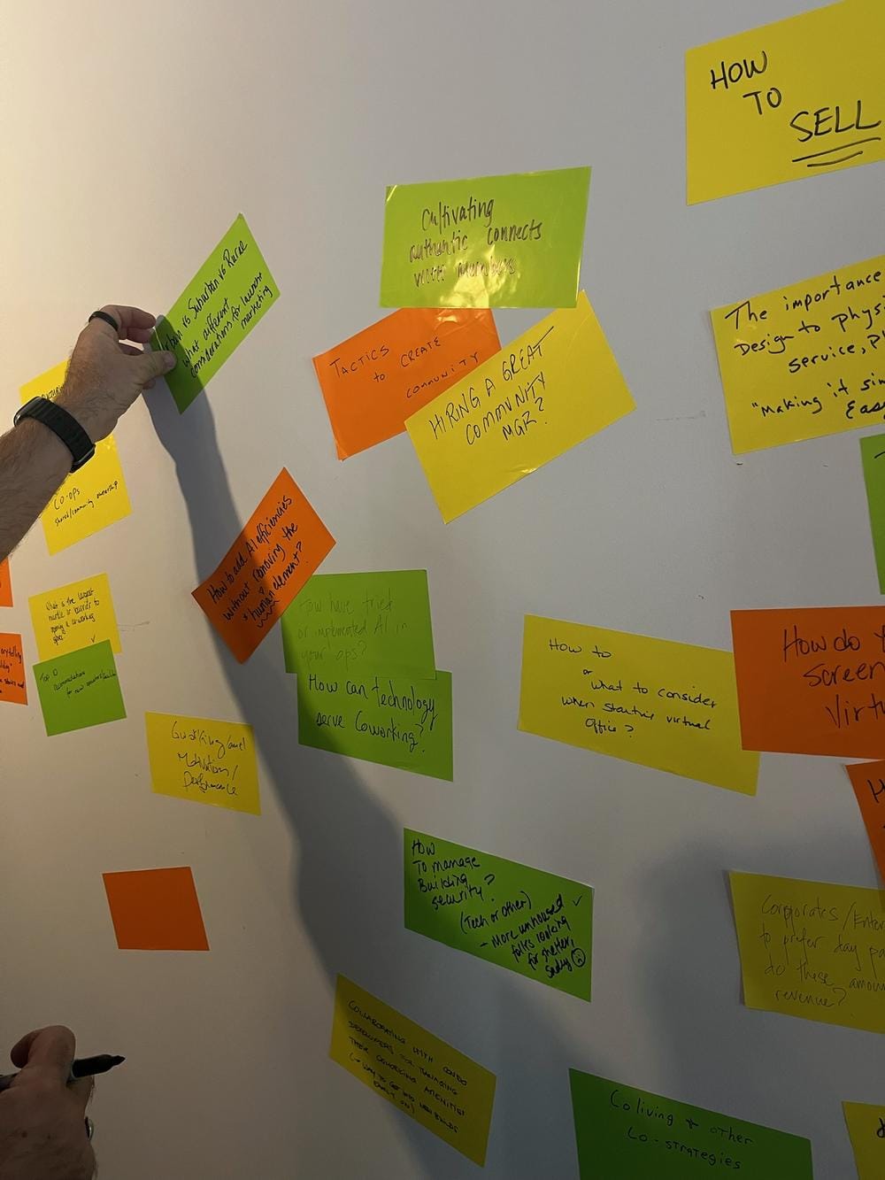 Unconference wall covered with handwritten orange, yellow, and green sticky notes proposing topics for Day 2 sessions