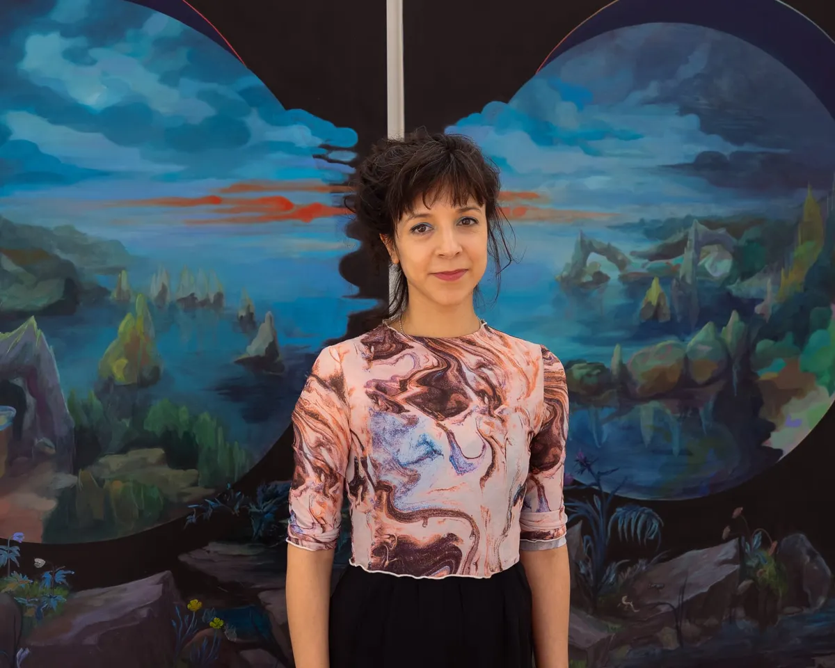 Anna Sebastian stands in front of her landscape paintings at IMT Gallery.