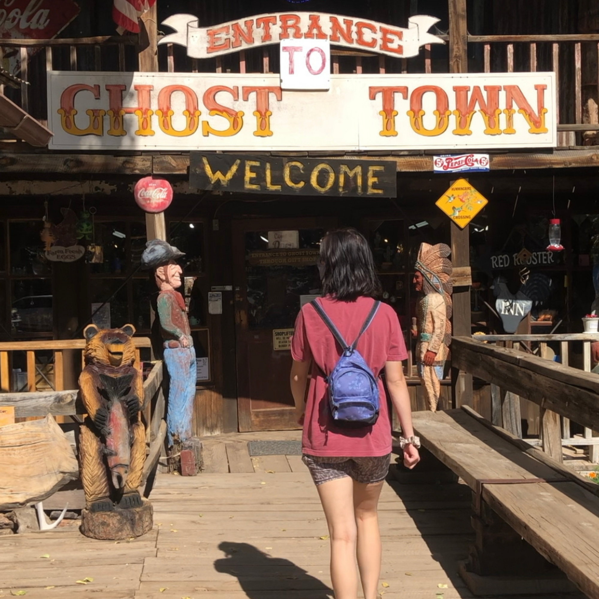 girl walking into tall wooden building with Gold King Mine & Ghost Town printed on the front