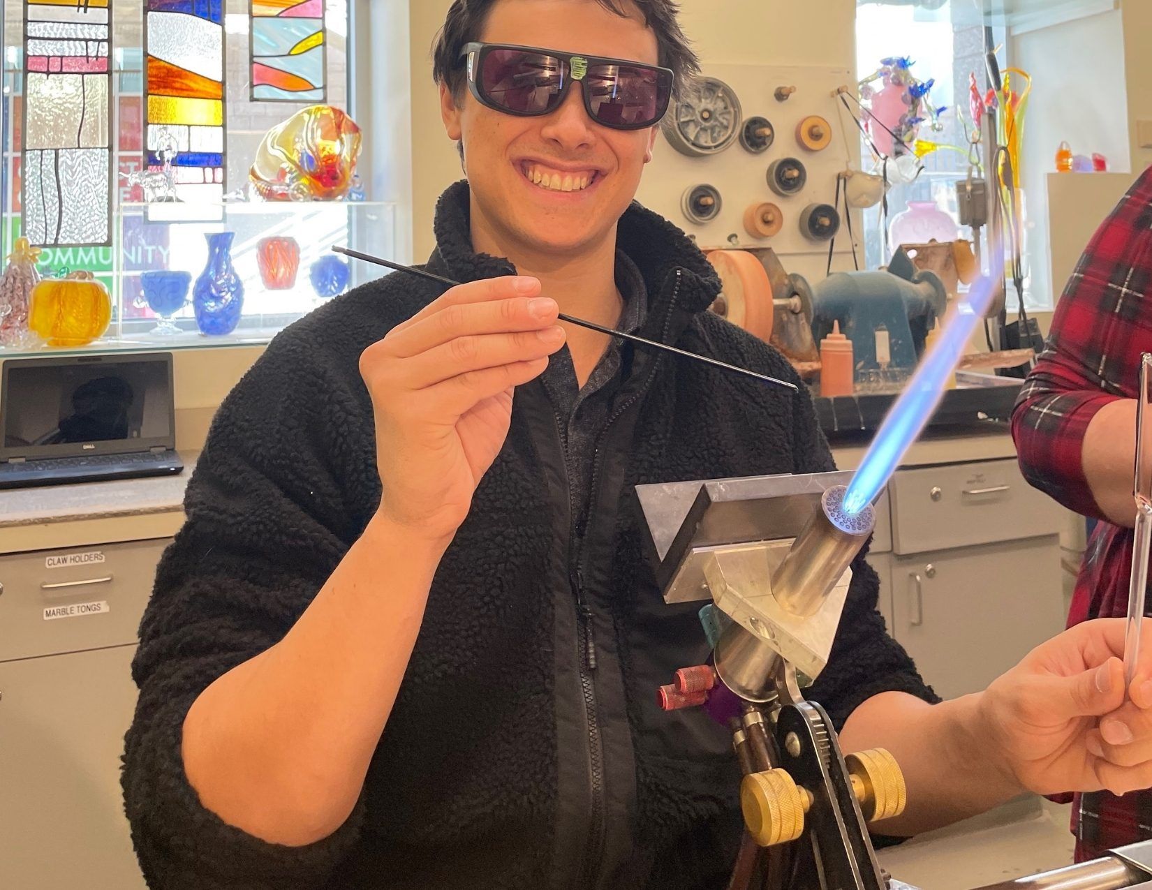 A young guy wearing safety goggles with a torch flame learning to blow glass.