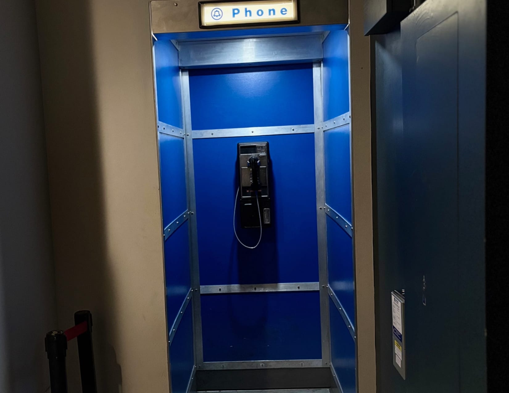 A hidden blue telephone booth with a vintage payphone inside, illuminated by cool blue lighting. 