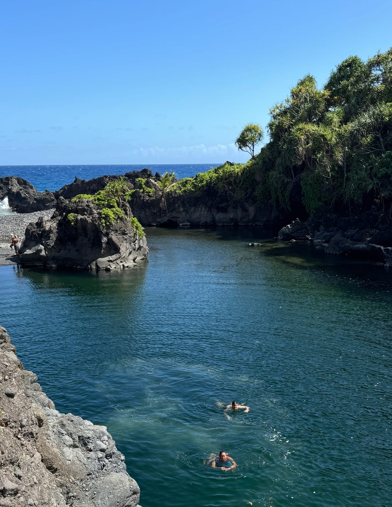 two people swimming in blue water overlooking the beach on the Road to Hana in Maui, Hawaii