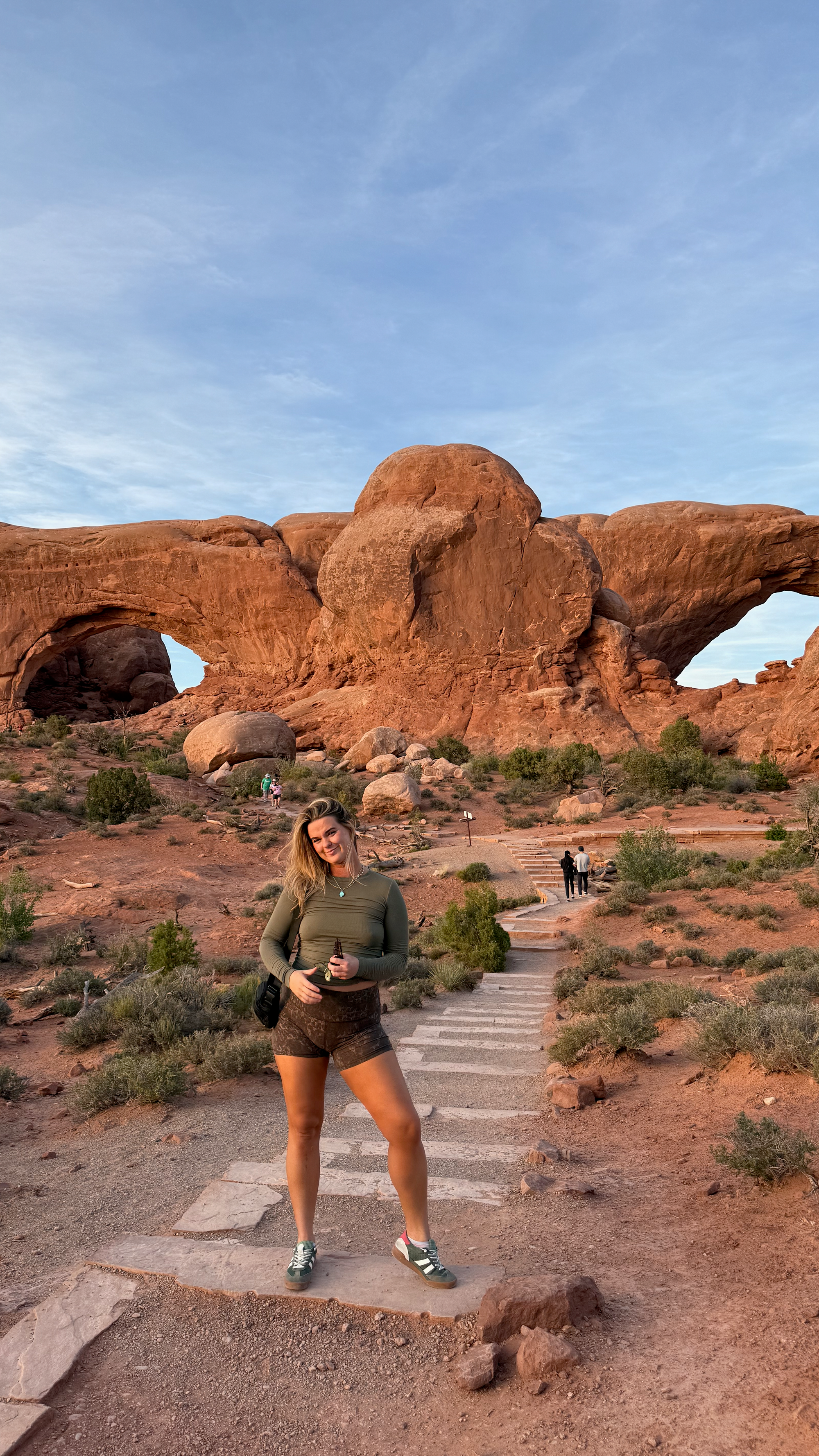 Woman in green shirt standing in front of the North Window Arch and South Window Arch at Arches National Park in Moab, Utah