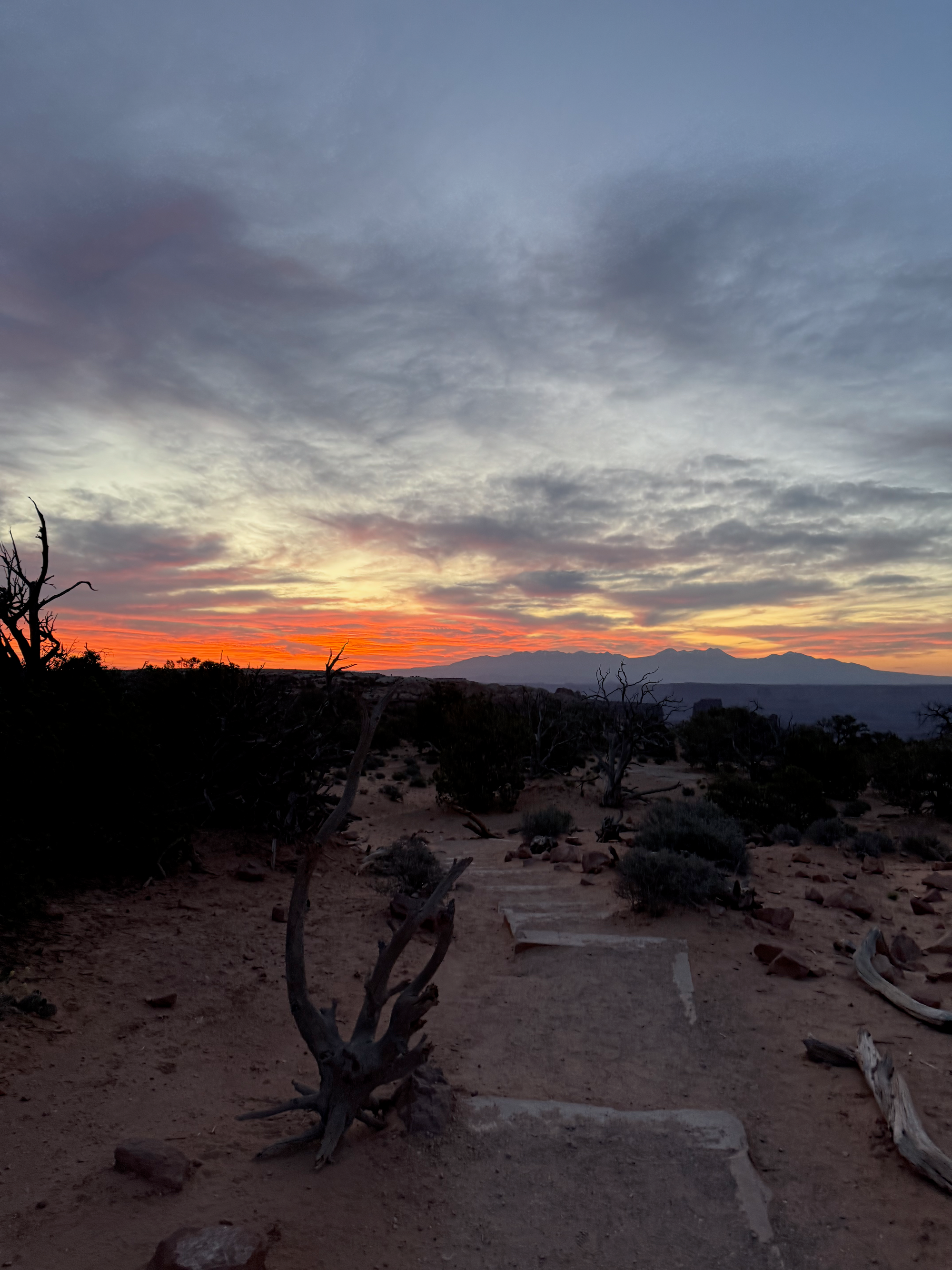 Hiking path with orange sunrise and mountain range in the background at the Mesa Arch Trailhead in Moab, Utah
