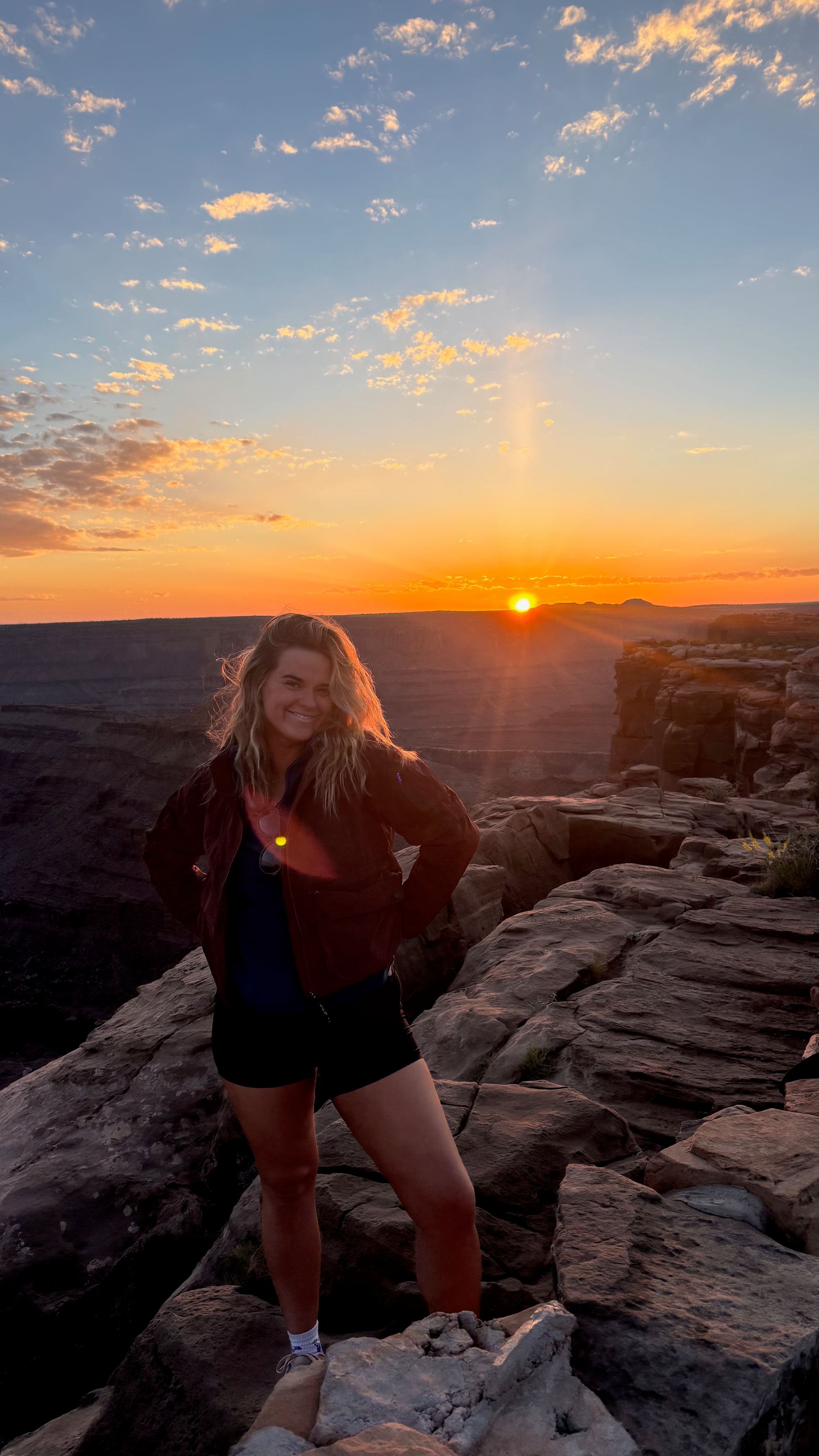 Woman standing on rocks near a cliff during sunset at Dead Horse Point State Park in Moab, Utah