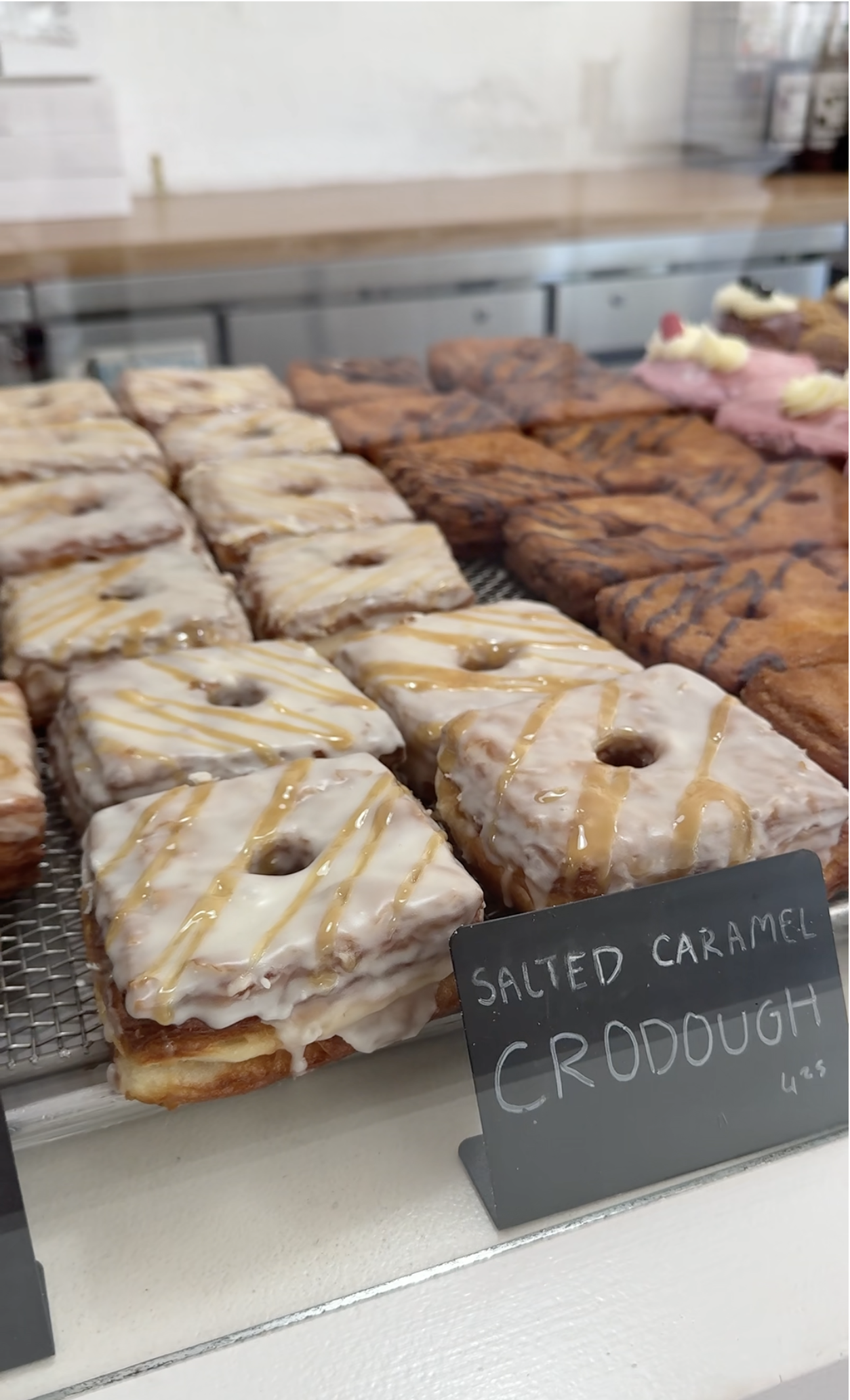 Over twenty square shaped donuts on display with a black sign labeled "Salted Caramel Crodough" at Doughbird in Moab, Utah